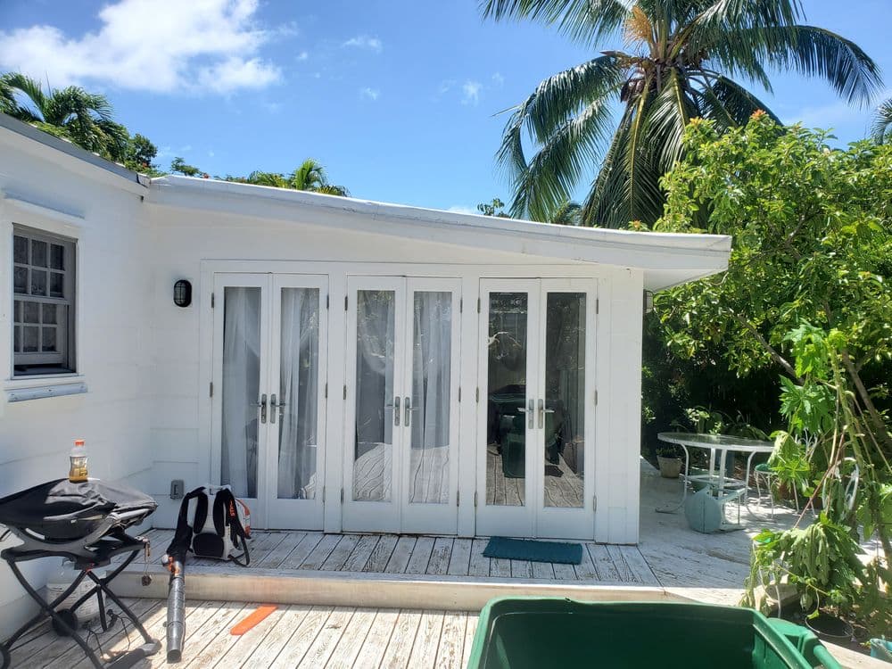 Modern white cottage with glass doors, surrounded by tropical plants and palm trees.
