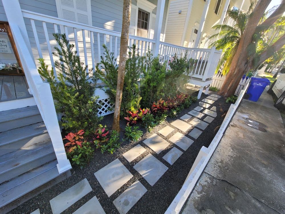 Colorful garden path with stone pavers, surrounded by lush plants outside a house.