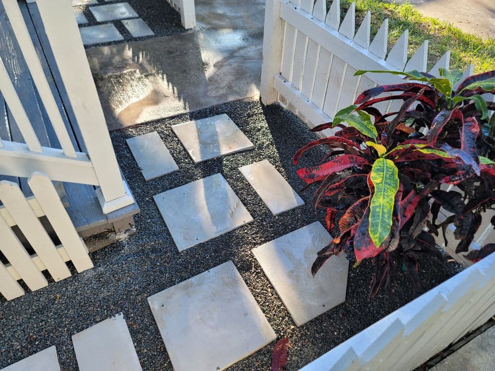 Garden pathway with concrete stepping stones and colorful foliage near a white picket fence.