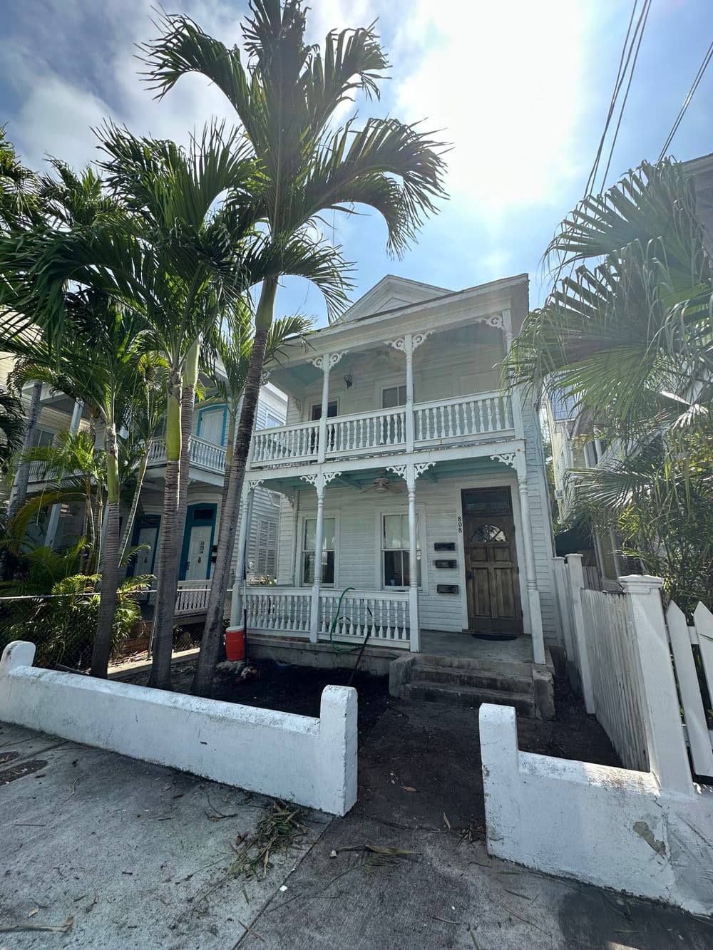Two-story coastal house with blue accents, surrounded by palm trees in sunny weather.