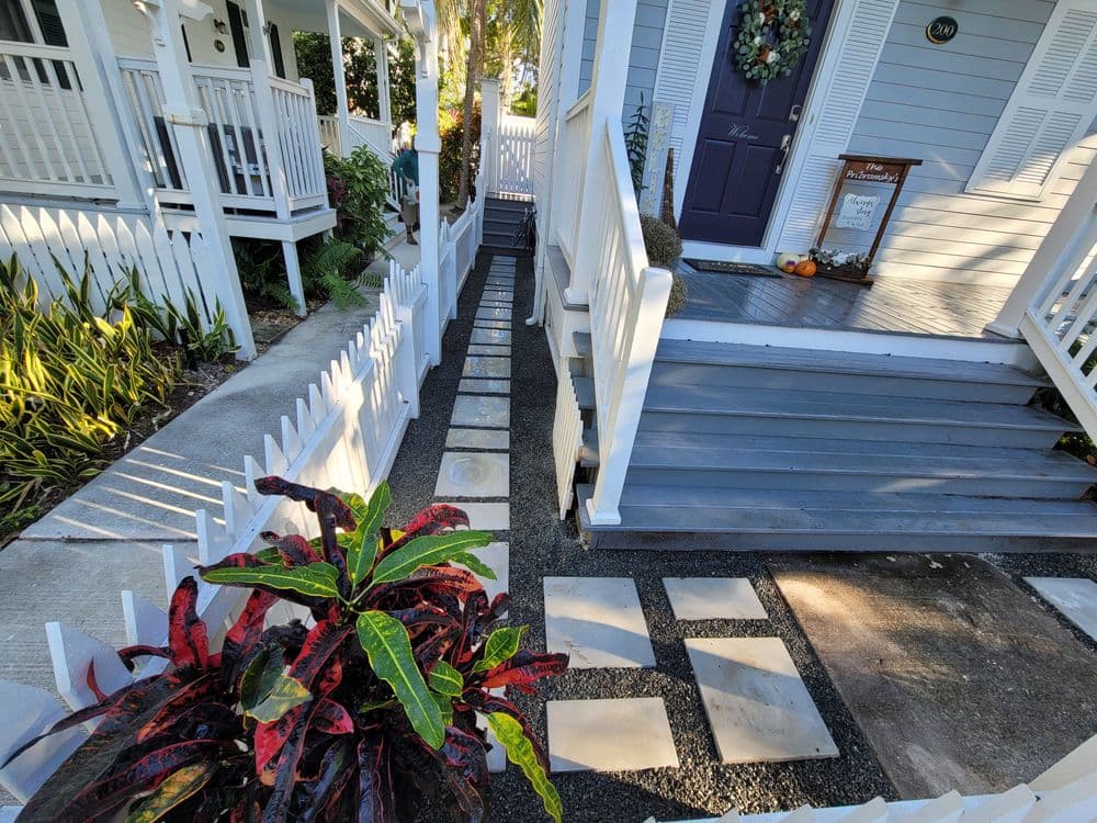 Charming walkway with stone path, colorful plants, and welcoming porch entrance.