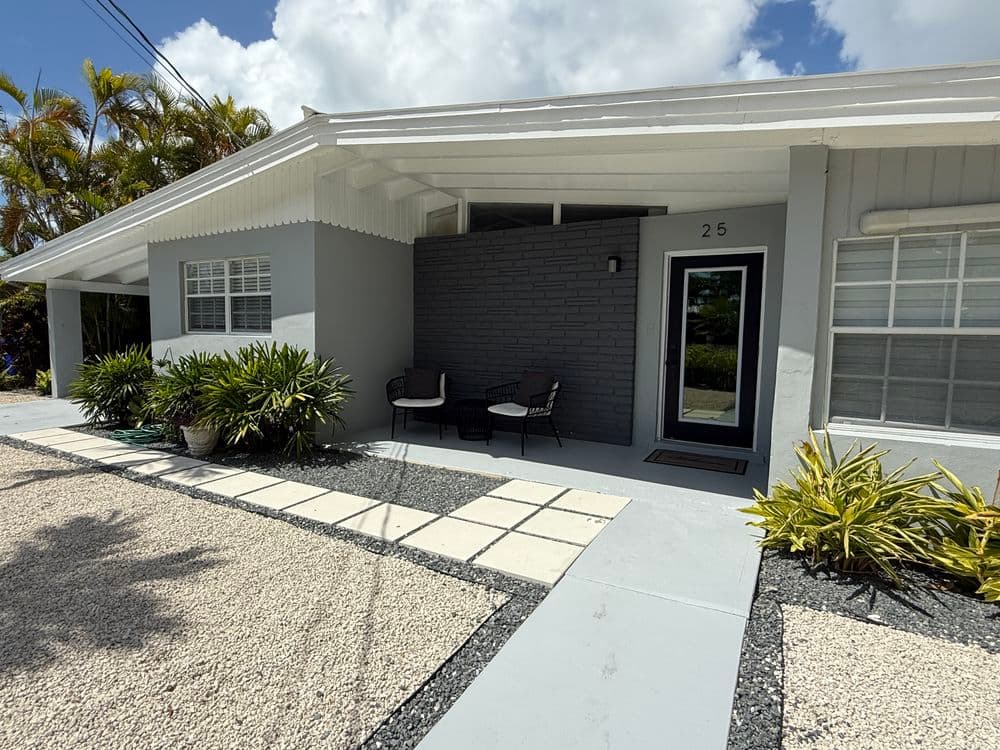 Modern home entrance with covered porch, stylish chairs, and tropical landscaping.