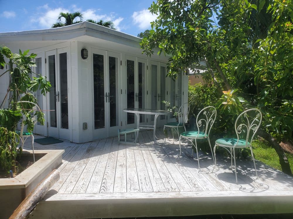 Charming outdoor patio with white furniture, greenery, and sunny sky, perfect for relaxation.