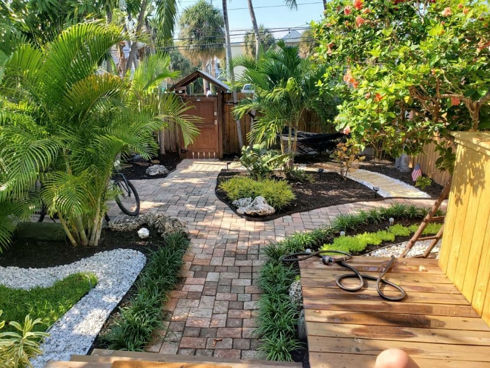 Lush tropical garden with brick path, greenery, and wooden deck creating a serene outdoor space.