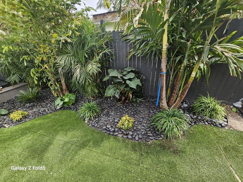 Lush garden with tropical plants, black stone borders, and artificial grass landscape design.