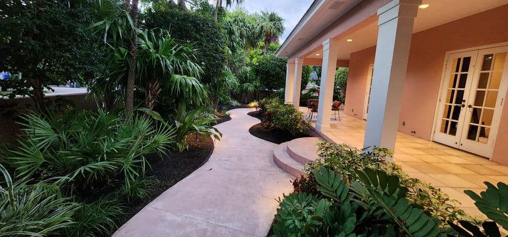 Curved pathway leading to a porch surrounded by lush tropical plants and greenery.