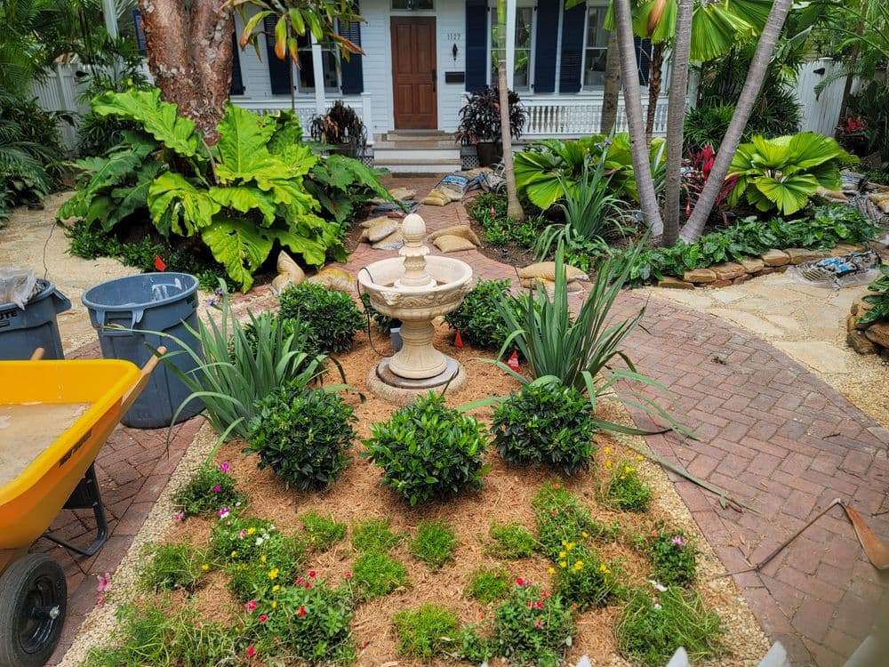 Garden landscape featuring a stone fountain surrounded by lush plants and colorful flowers.
