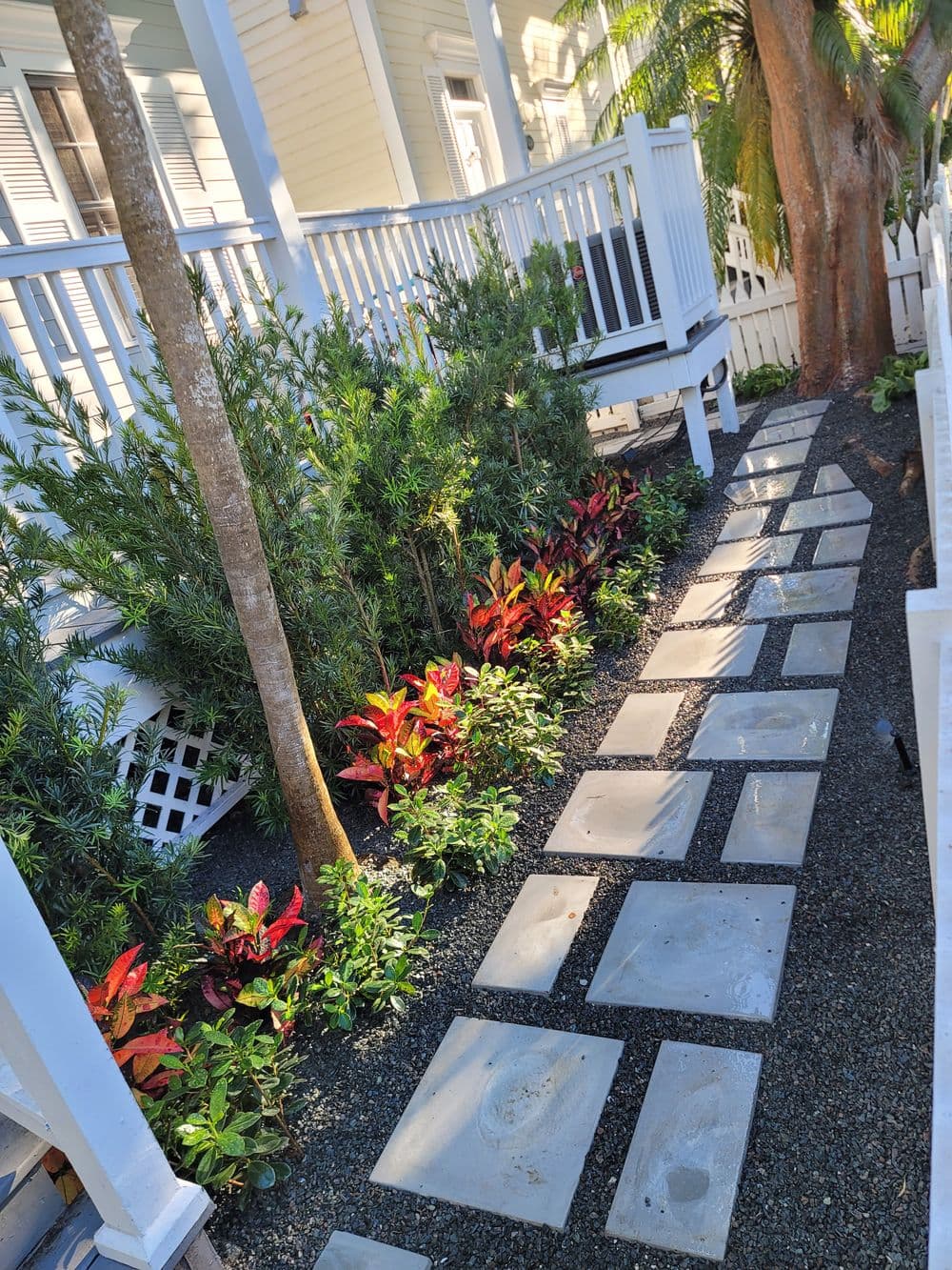 Lush garden path with colorful plants and stepping stones by a house porch.