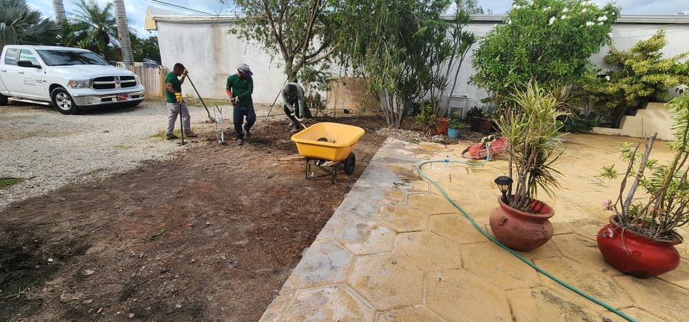 Landscaping workers using tools and a wheelbarrow to prepare a garden area.